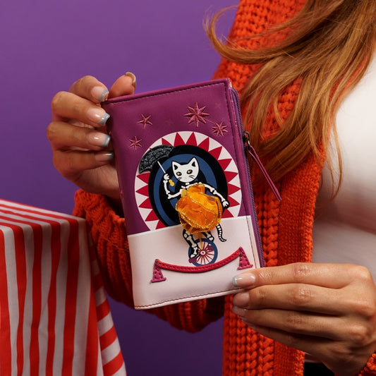 Person holding a purple wallet with a cat design against a purple background