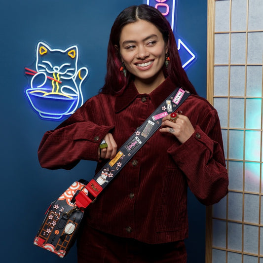 Person holding a colorful bag with a neon sign of a cat eating noodles in the background