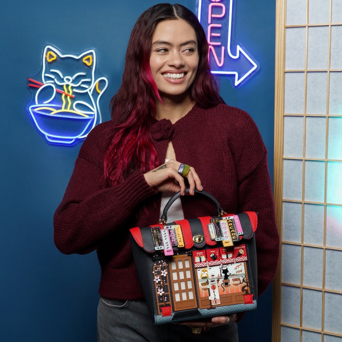 Person holding a unique handbag with various designs against a blue wall with neon signs.