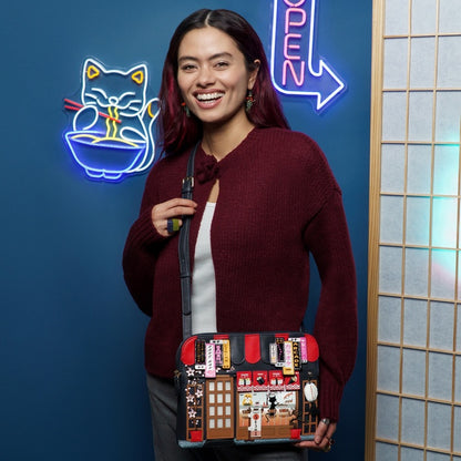 Woman holding a unique handbag with a colorful design, standing in front of a blue wall with neon signs.