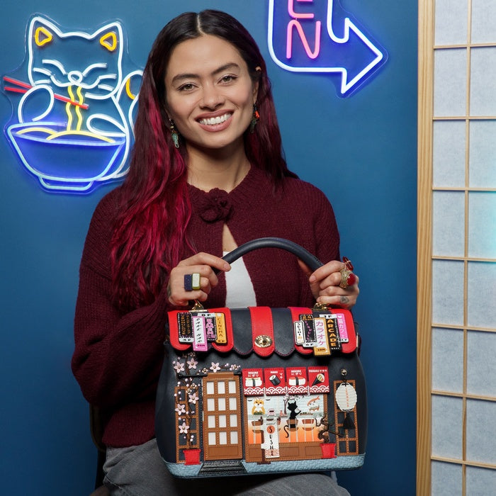 Woman holding a unique handbag with a building design against a blue wall with neon signs.