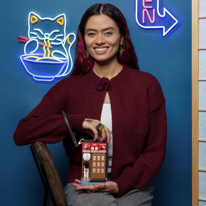 Woman holding a small model of a building in front of a blue wall with neon signs.