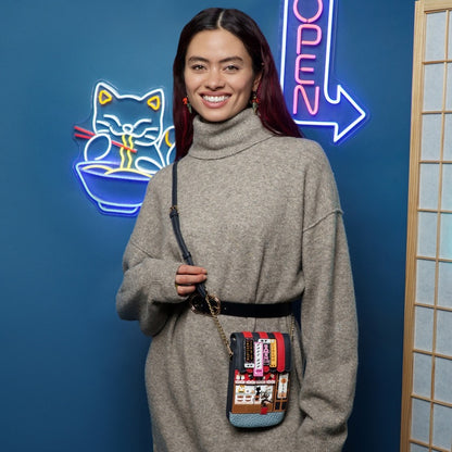 Woman holding a colorful crossbody bag in front of a blue wall with neon signs.