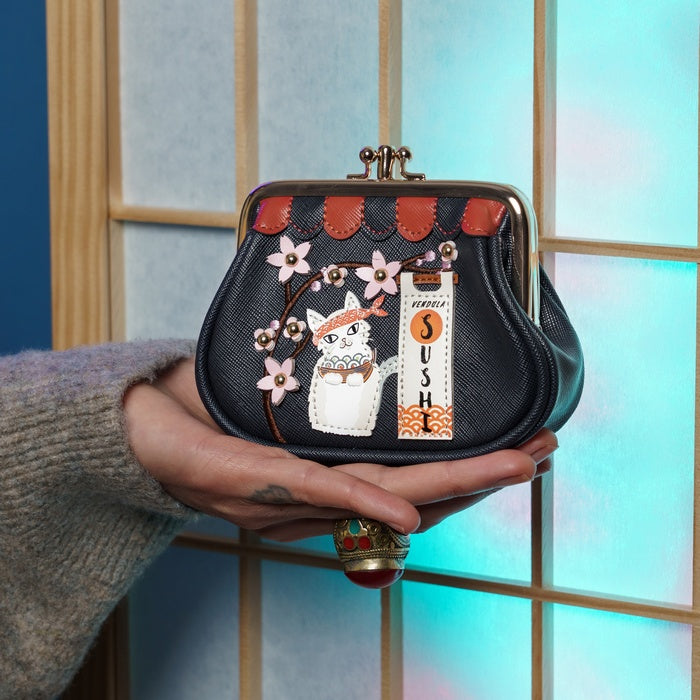 Hand holding a black purse with cat design and 'SUSHI' text against a blurred window background
