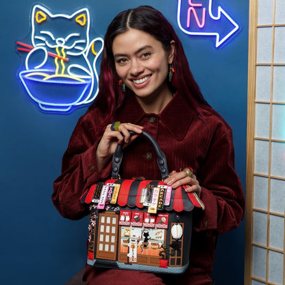 Woman holding a unique handbag with a colorful design against a blue wall with neon signs.