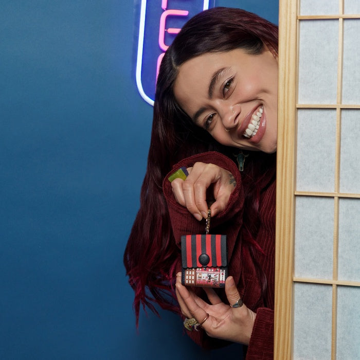 Woman holding a small red and black bag against a blue wall with neon lights.