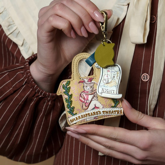 Person holding a keychain with a design of Shakespeare's Theatre and a cat in a hat.