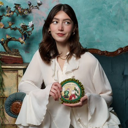 Woman holding a decorative plate in a room with a blue wall and ornate furniture.