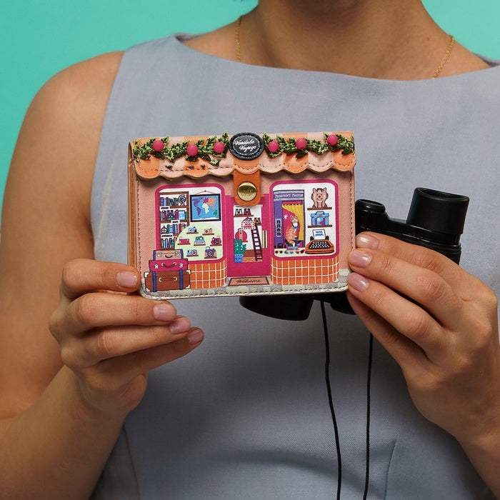 Person holding a small, intricately designed model of a store front with a teal background.