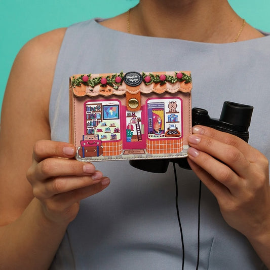 Person holding a small, intricately designed model of a store front with a teal background.