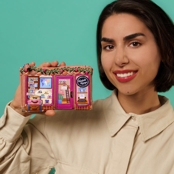 Woman holding a colorful miniature book-shaped house against a teal background