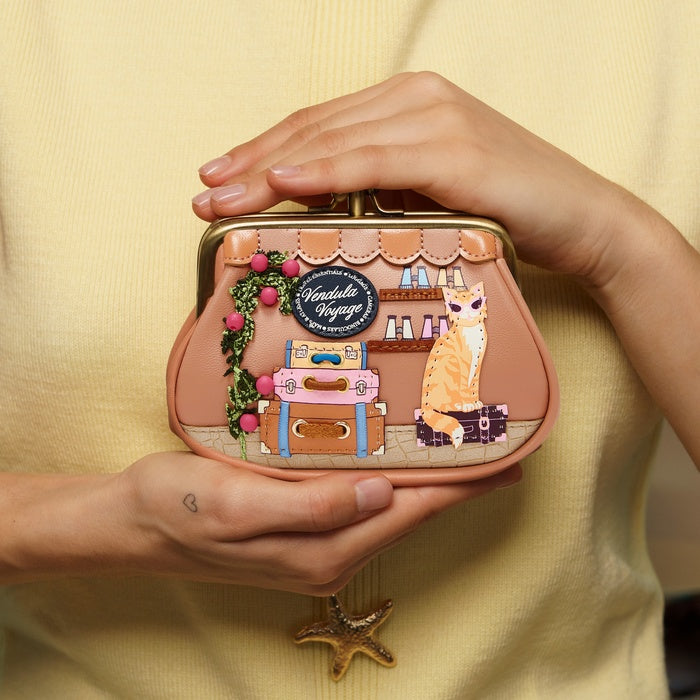 Person holding a small pink handbag with travel-themed design against a yellow background