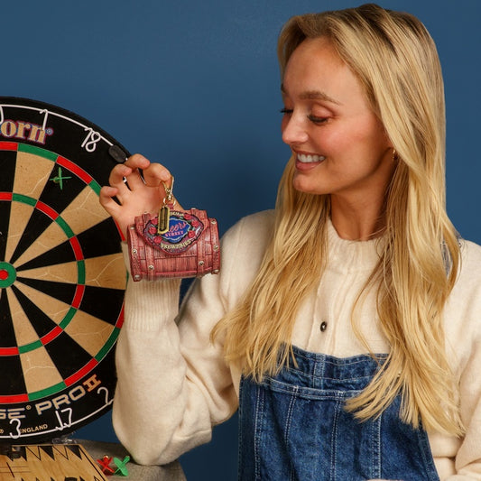 Woman holding a small red purse with a keychain, standing next to a dartboard against a blue background