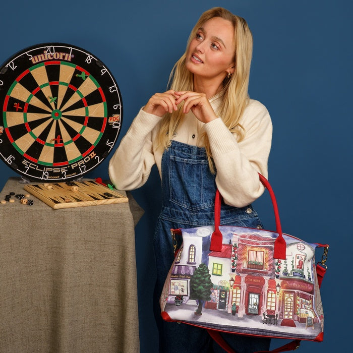 Woman holding a tote bag with a street scene design next to a dartboard on a blue background
