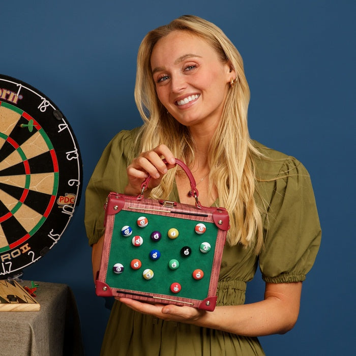Woman holding a handbag with pool ball designs next to a dartboard on a blue background