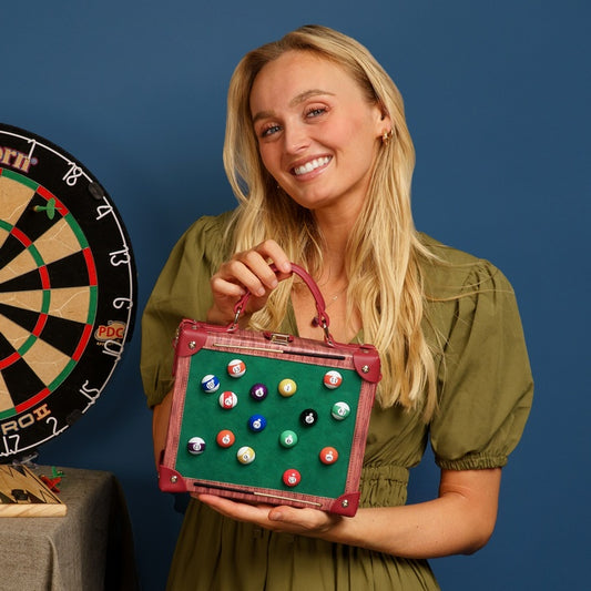 Woman holding a handbag with pool ball designs next to a dartboard on a blue background