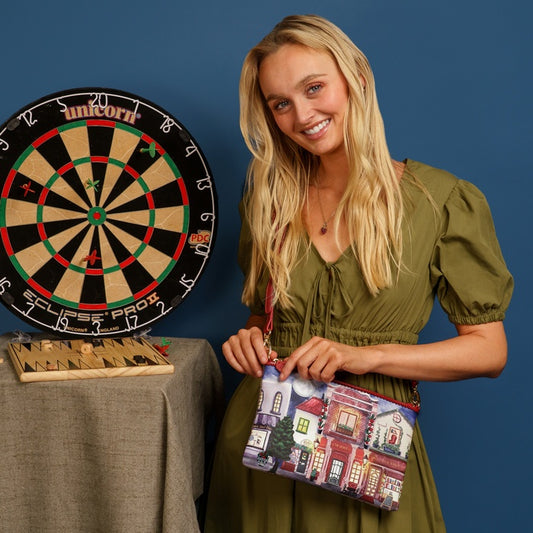 Woman holding a colorful clutch next to a dartboard on a blue background