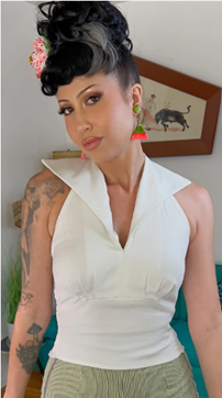 Woman wearing a white sleeveless top with a high collar, standing indoors.