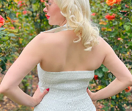 Woman in a white dress standing outdoors with flowers in the background