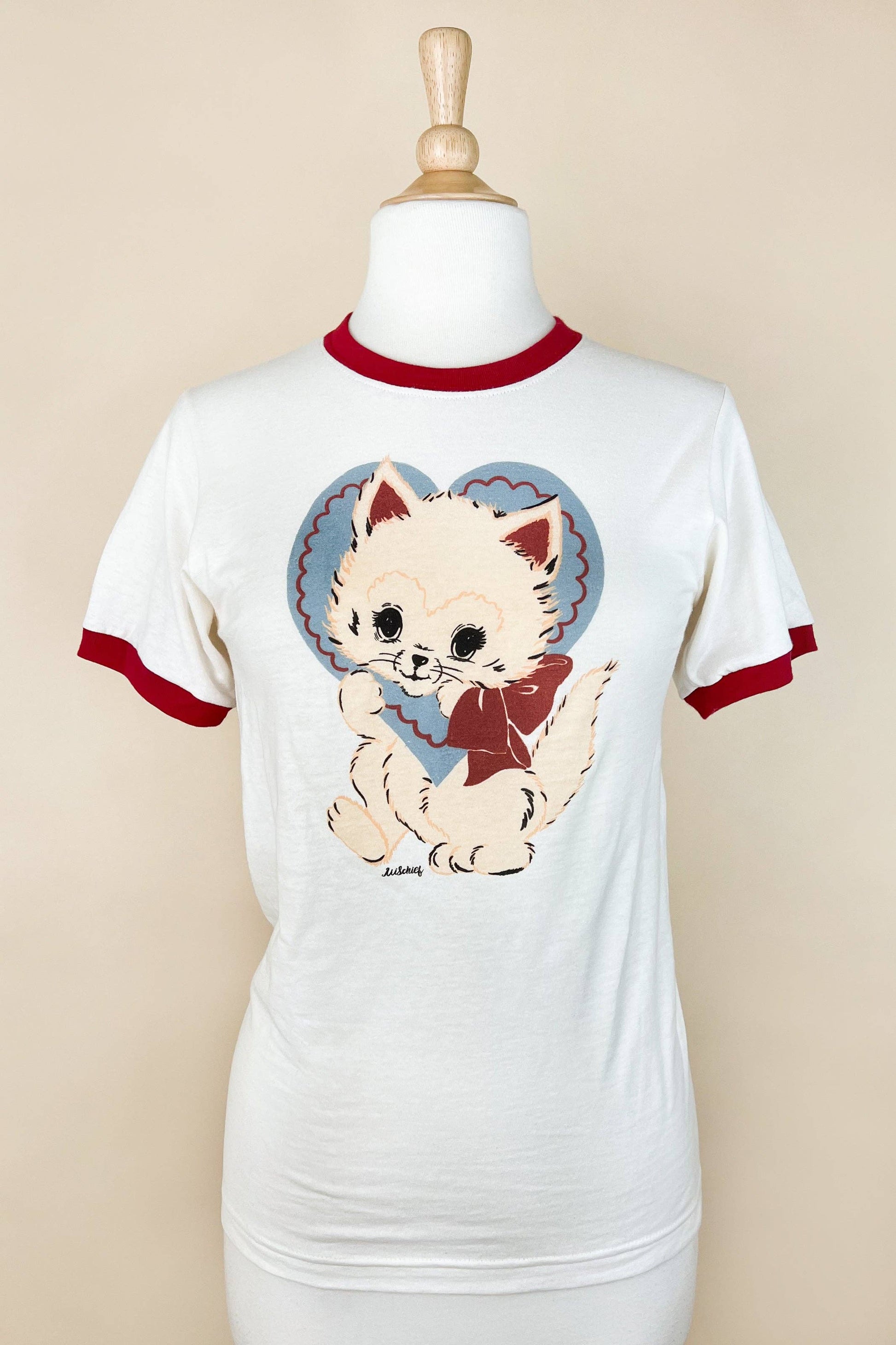 White t-shirt with red ringer sleeves featuring a cartoon cat design on a mannequin against a beige background.
