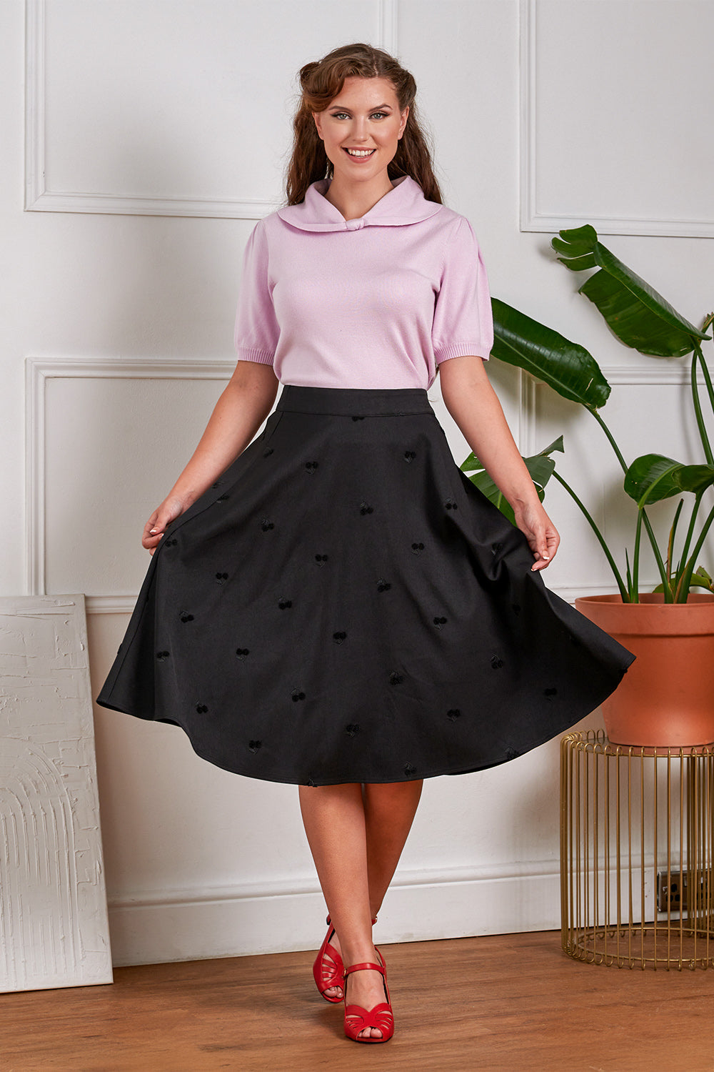 Woman wearing a pink top and black skirt with heart patterns indoors.