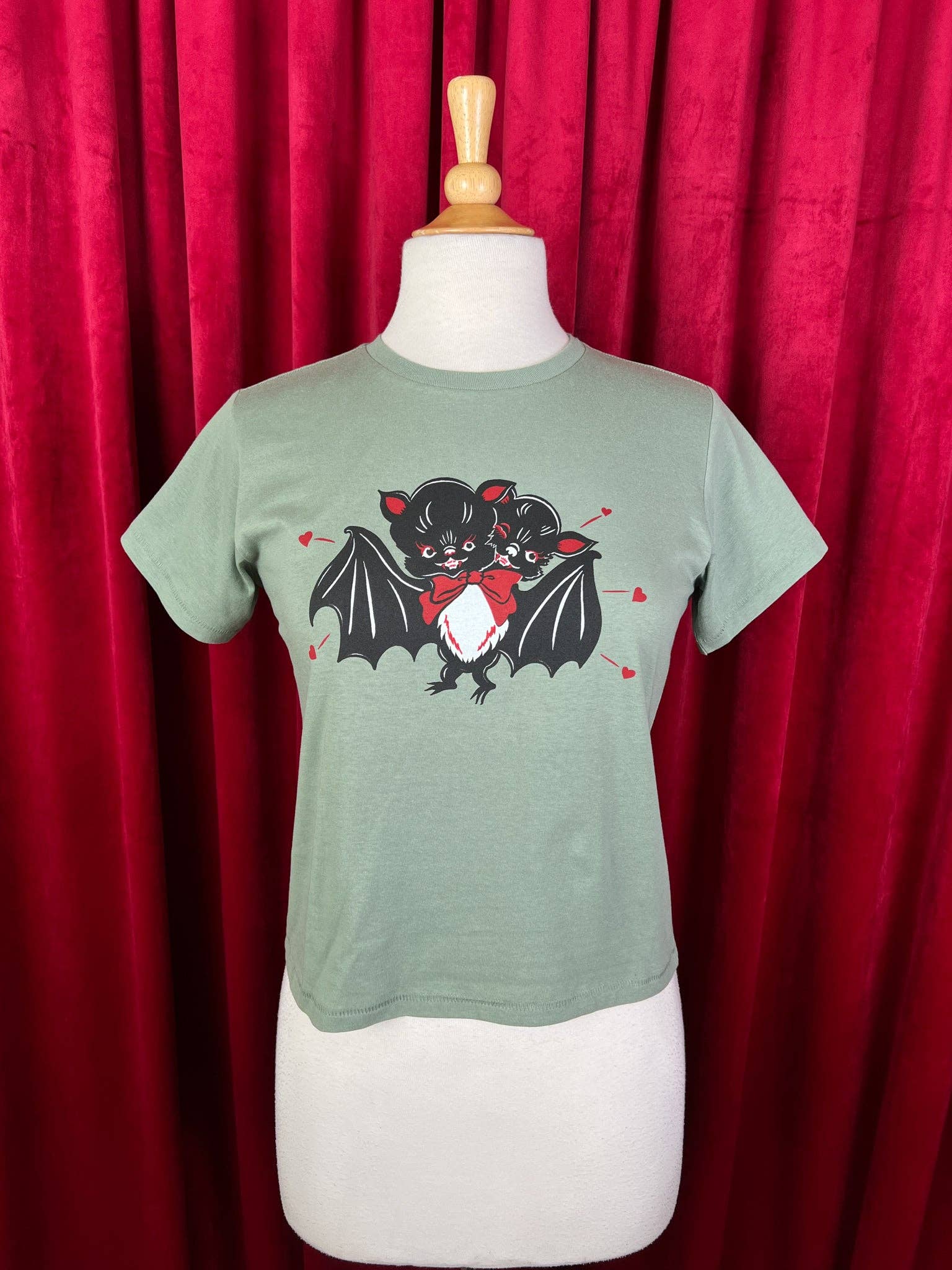 Green t-shirt with bat design on a mannequin against a red curtain background