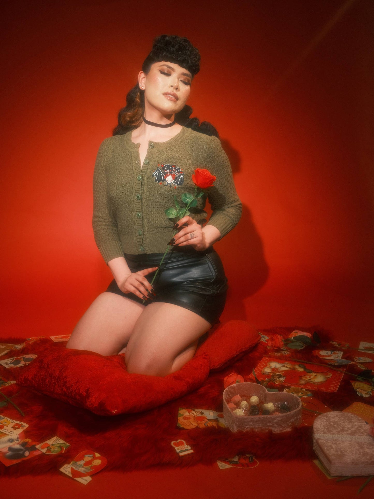 Woman sitting on a red pillow holding a red rose against a red background
