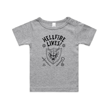A close-up of a white garment, likely a t-shirt, featuring a black graphic print. The design displays the text 'HELLFIRE LIVES!' in a distressed, arched font above a horned skull inside a shield, surrounded by fantasy icons including dice, a sword, a key, and a gem.