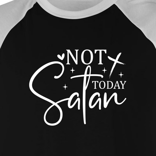 A close-up of a raglan-style baseball t-shirt featuring a black body and white sleeves, with a white graphic print on the front that reads 'NOT TODAY Satan' in stylized lettering.