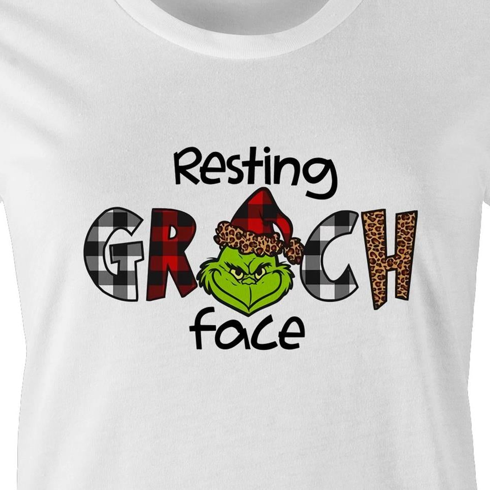 White crewneck t-shirt featuring a graphic print of the Grinch wearing a red and black plaid Santa hat, with the text 'Resting GRCH face' in black.