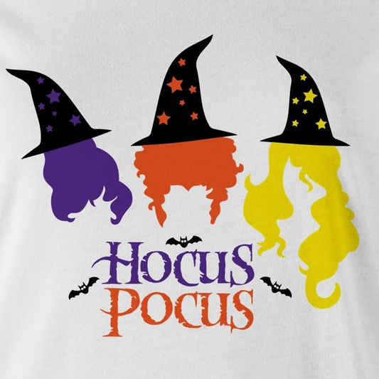A close-up of a white fabric surface featuring a colorful Halloween graphic with three witch hats and flowing hair in purple, orange, and yellow, plus the words 'Hocus Pocus' and small bat silhouettes.