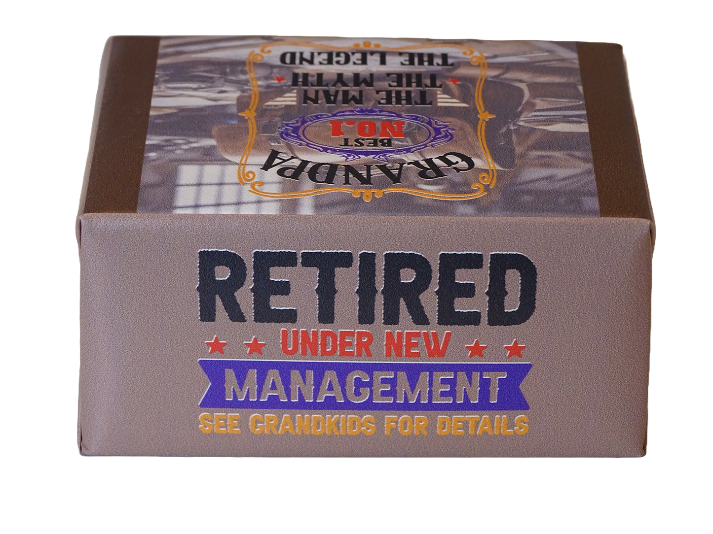 A rectangular product box with a brown and gray design, featuring the text 'RETIRED UNDER NEW MANAGEMENT' and 'SEE GRANDKIDS FOR DETAILS' on a white background.