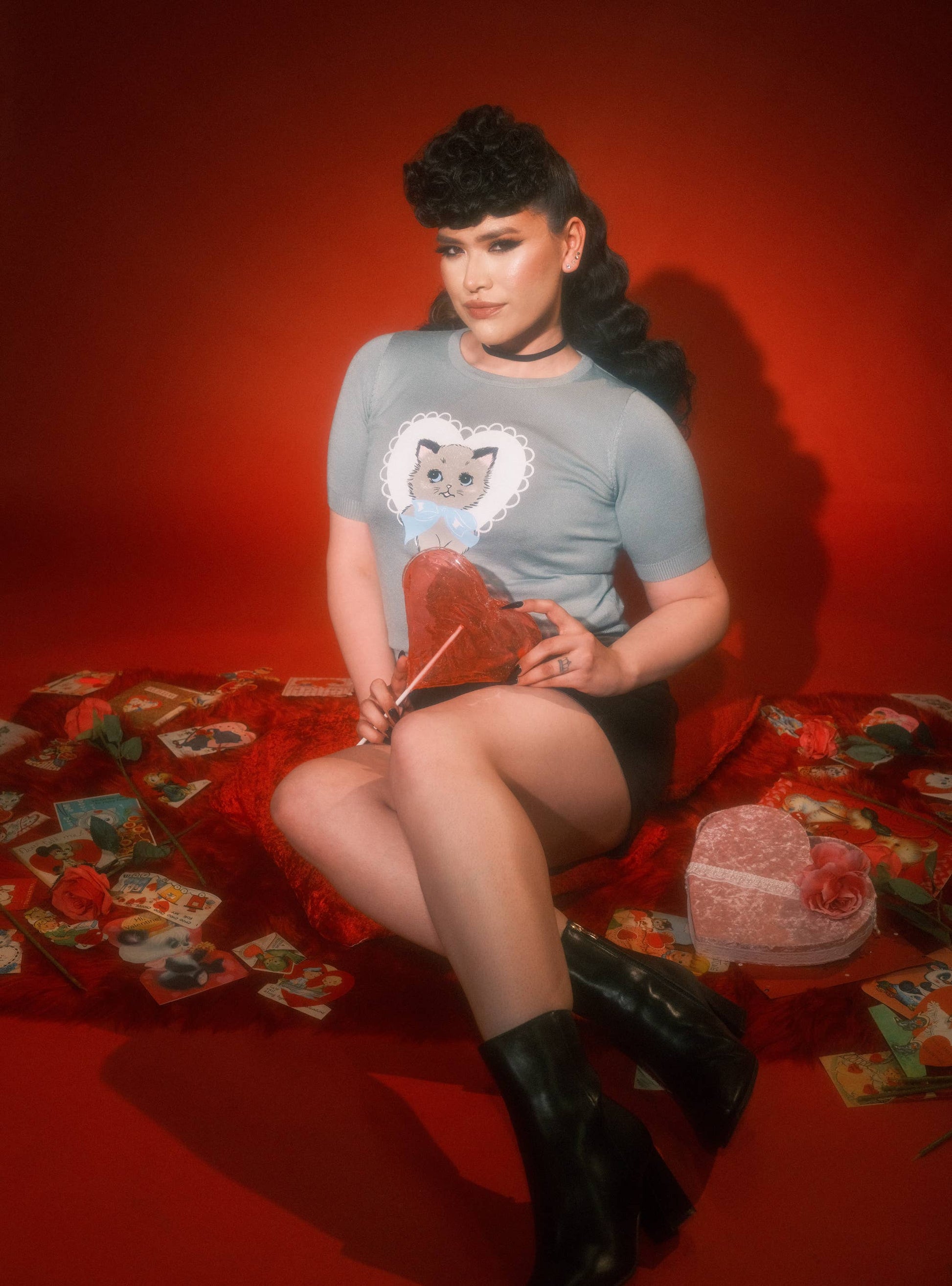 Person wearing a gray t-shirt with a cat design, sitting on a red surface with playing cards.