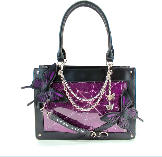 Black leather handbag with a purple glitter spiderweb pattern panel, black butterfly appliqués, silver chain details, and a black shoulder strap on a white background.