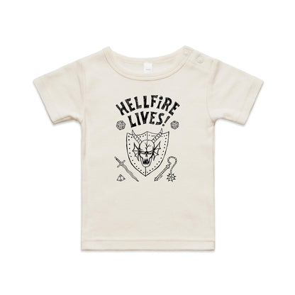 A close-up of a white garment, likely a t-shirt, featuring a black graphic print. The design displays the text 'HELLFIRE LIVES!' in a distressed, arched font above a horned skull inside a shield, surrounded by fantasy icons including dice, a sword, a key, and a gem.