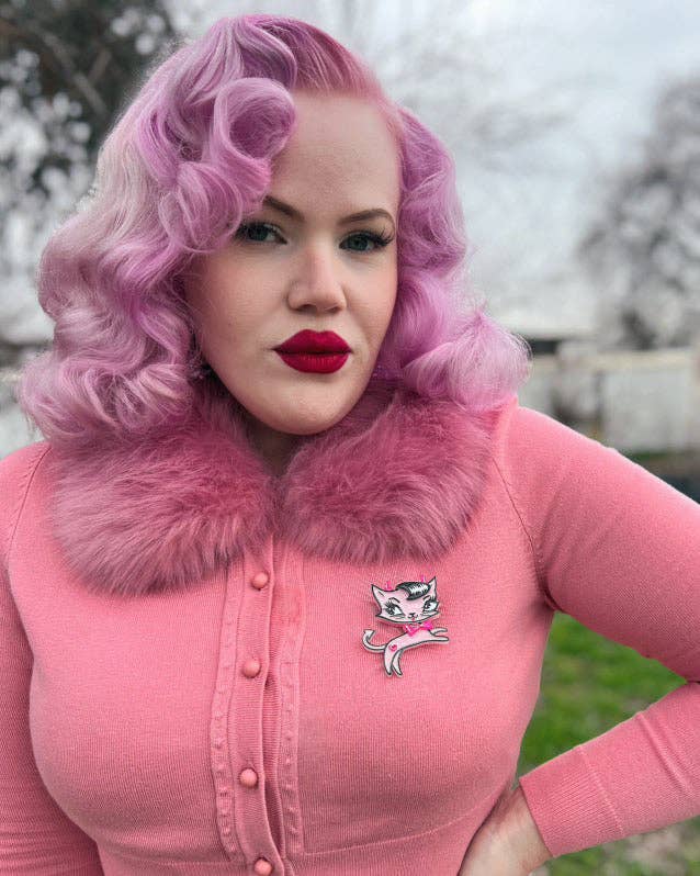 Woman with pink hair and red lipstick wearing a pink outfit with a cat logo.
