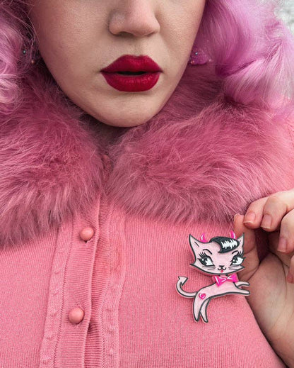 A close-up lifestyle shot of a person wearing a pink cardigan with a fluffy pink fur collar, featuring a retro-style cartoon cat pin on the chest.