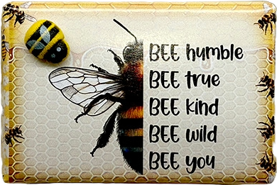 A square decorative plaque or sign featuring a large black-and-yellow bumblebee illustration, a small bee at upper left, honeycomb border details, and the phrase 'BEE humble BEE true BEE kind BEE wild BEE you' printed on a light background.