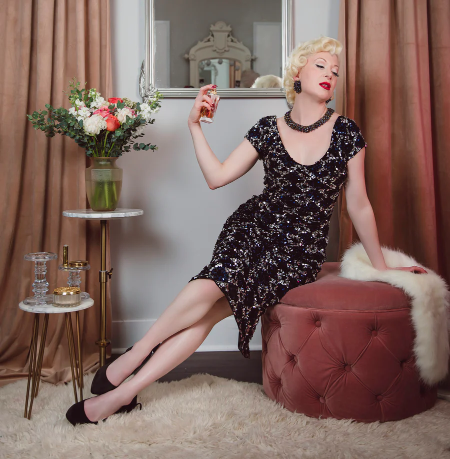 Woman in a black floral dress sitting on a red ottoman with a bouquet of flowers in the background.