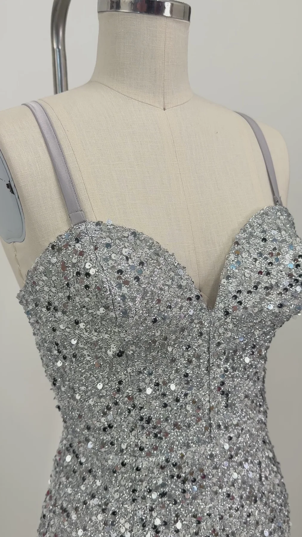 A close-up of a silver sequined strap dress displayed on a beige fabric mannequin torso against a plain light background.