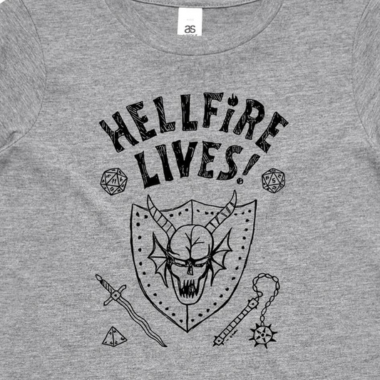 A close-up of a heather gray t-shirt featuring a black graphic print of a horned skull in a shield, surrounded by fantasy-themed icons including dice, a sword, and a mace, with the text 'HELLFIRE LIVES!'.