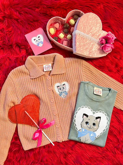 Cardigan, t-shirt, and heart-shaped box on a red textured surface