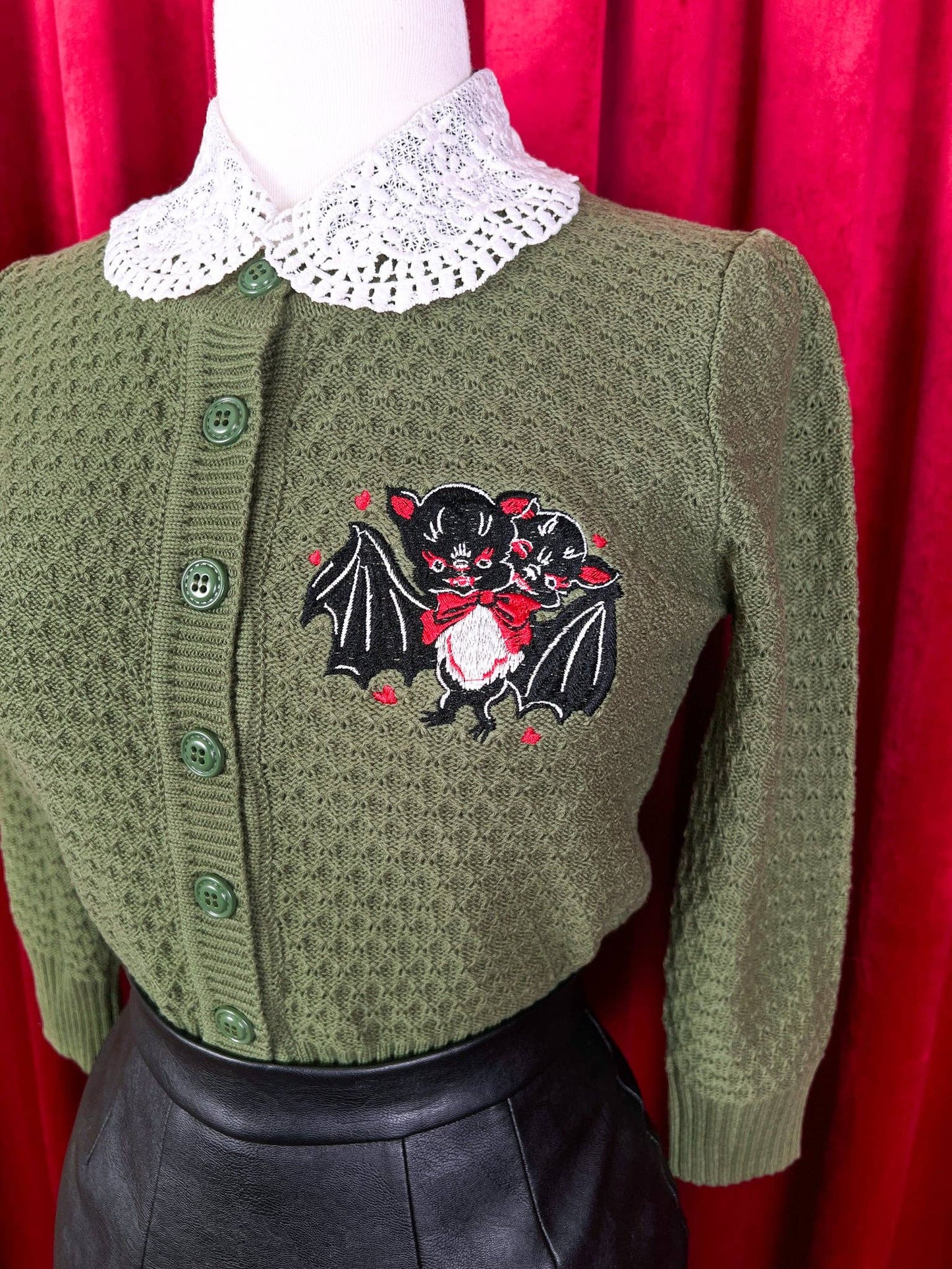 Green cardigan with a bat design on a red curtain background