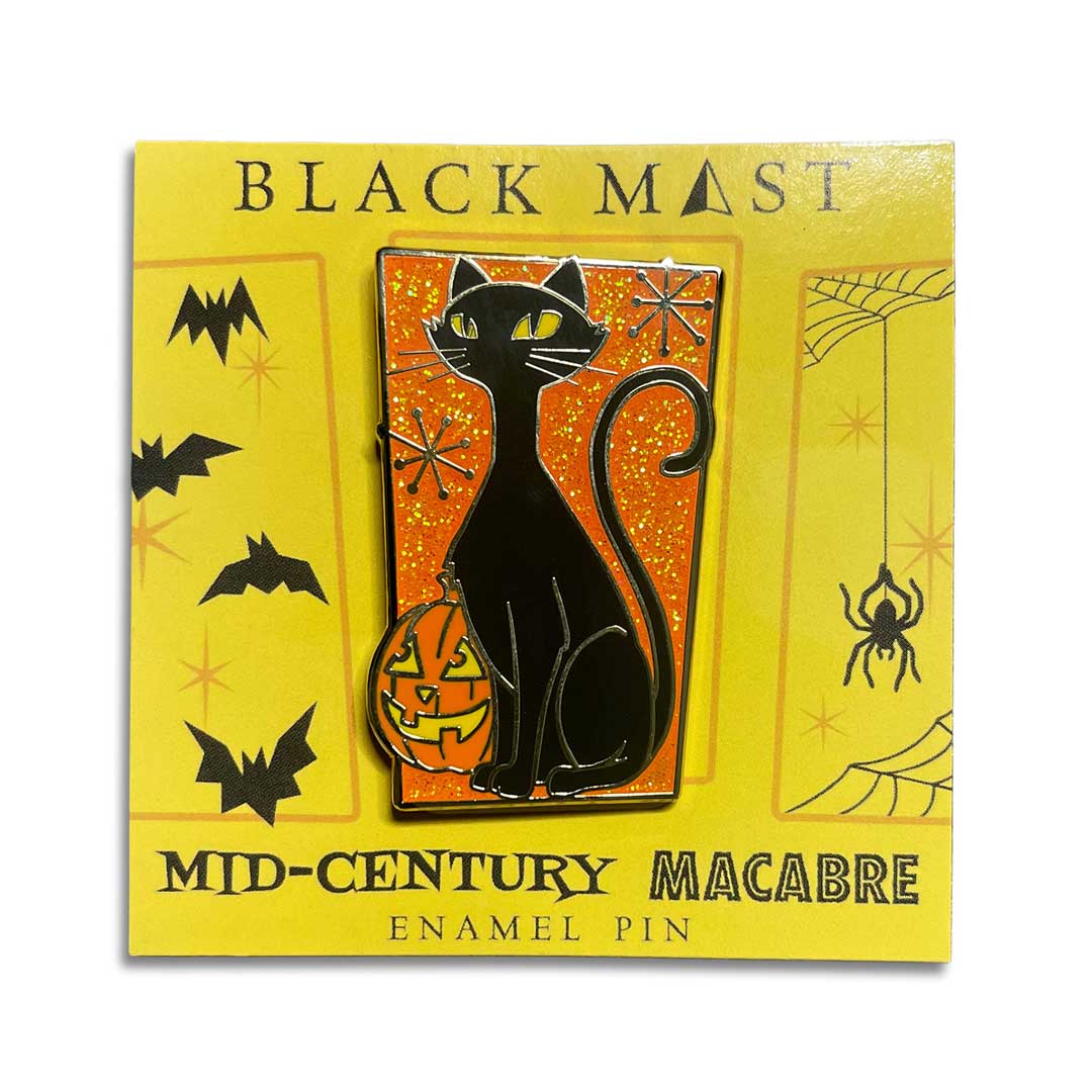 A Halloween enamel pin featuring a black cat sitting on a glowing orange pumpkin against an orange glittery background, mounted on a yellow retail card labeled 'BLACK MAEST' and 'MID-CENTURY MACABRE ENAMEL PIN'.