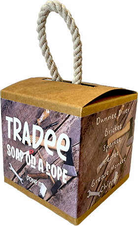 A square kraft paper soap box with a thick rope handle, featuring a rustic wood-grain label that reads 'TRADEE SOAP OR A ROPE' and lists scent names including 'Dannee River', 'Briquette', 'Spice', 'Meringue', and 'Chileño' on the side.