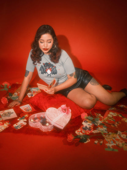 Woman sitting on a red floor with tarot cards and a heart-shaped box against a red background