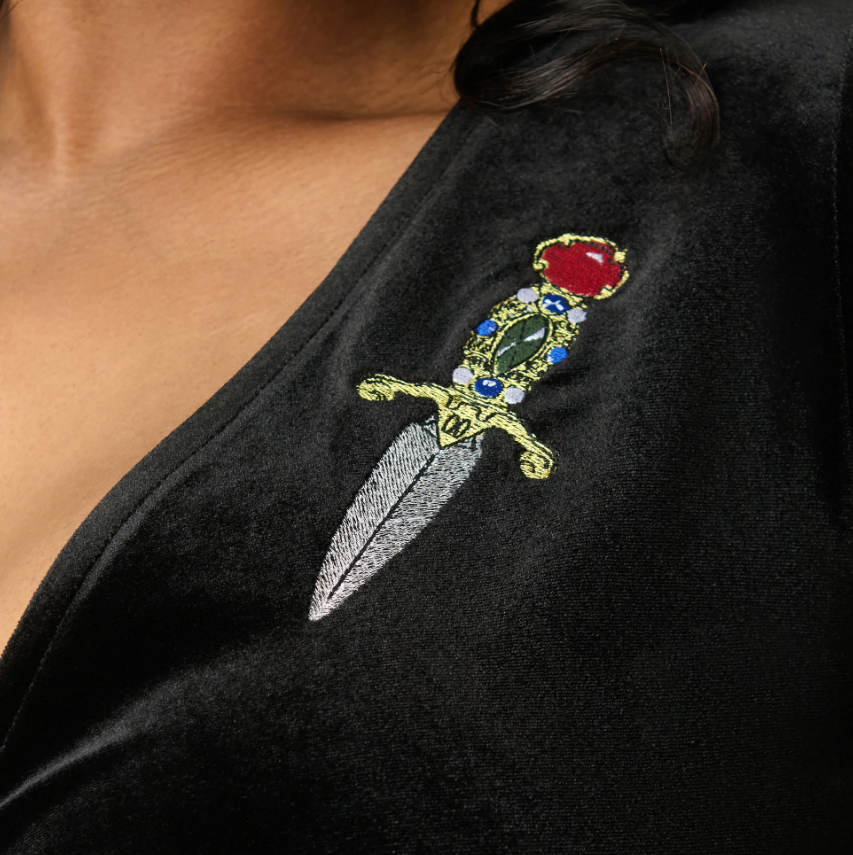 Black garment with an embroidered design of a sword and rose on a person's shoulder.