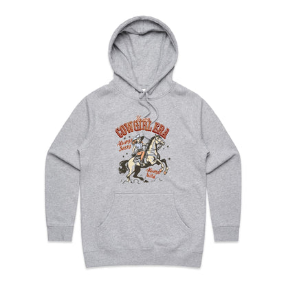 A close-up of a light heather gray hoodie featuring a vintage-style graphic of a cowboy riding a horse, with the text 'In my COWGIRL ERA Always Sassy Always Wild'.