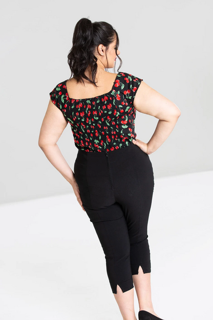 Woman wearing a black top with red cherry pattern and black pants on a white background