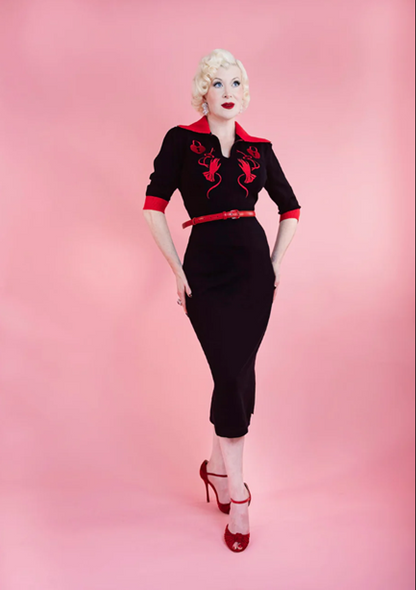 Woman wearing a black dress with red accents on a pink background